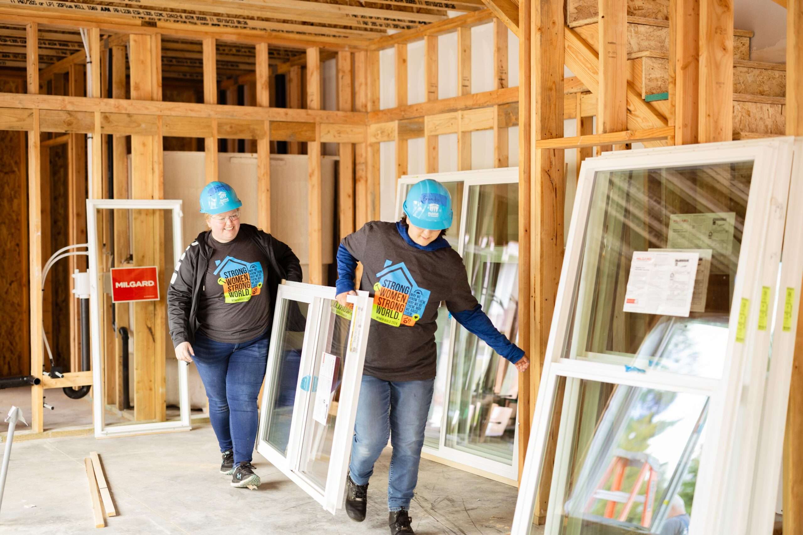Two women carrying a new window on a construction site.